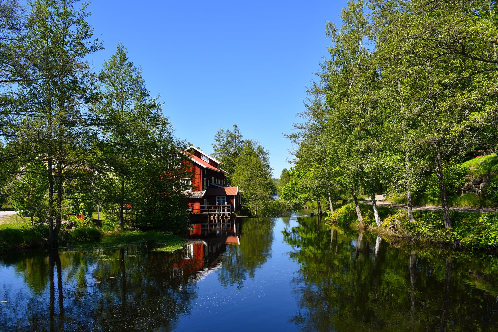 Foto från Mörtfors med en å och ett rött hus i förgrunden